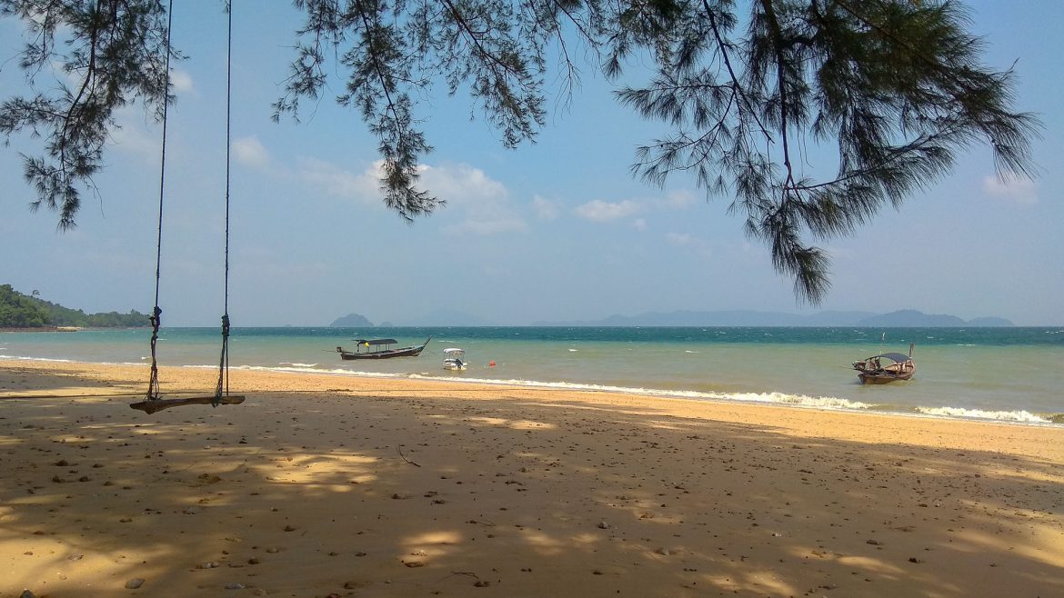 Der Sandstrand Aow Mook mit ein paar Booten im seichten Meer und einer Schaukel, die an einem hohen Baum hängt