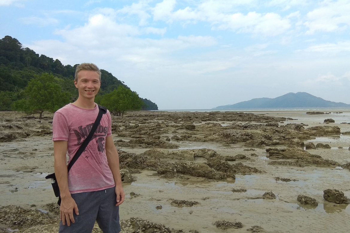 Markus am Stand Aow Pai bei Ebbe. Die Felsen ragen aus dem Sand und selbst der Baum der im Wasser hätte sein sollen, steht am Strand.