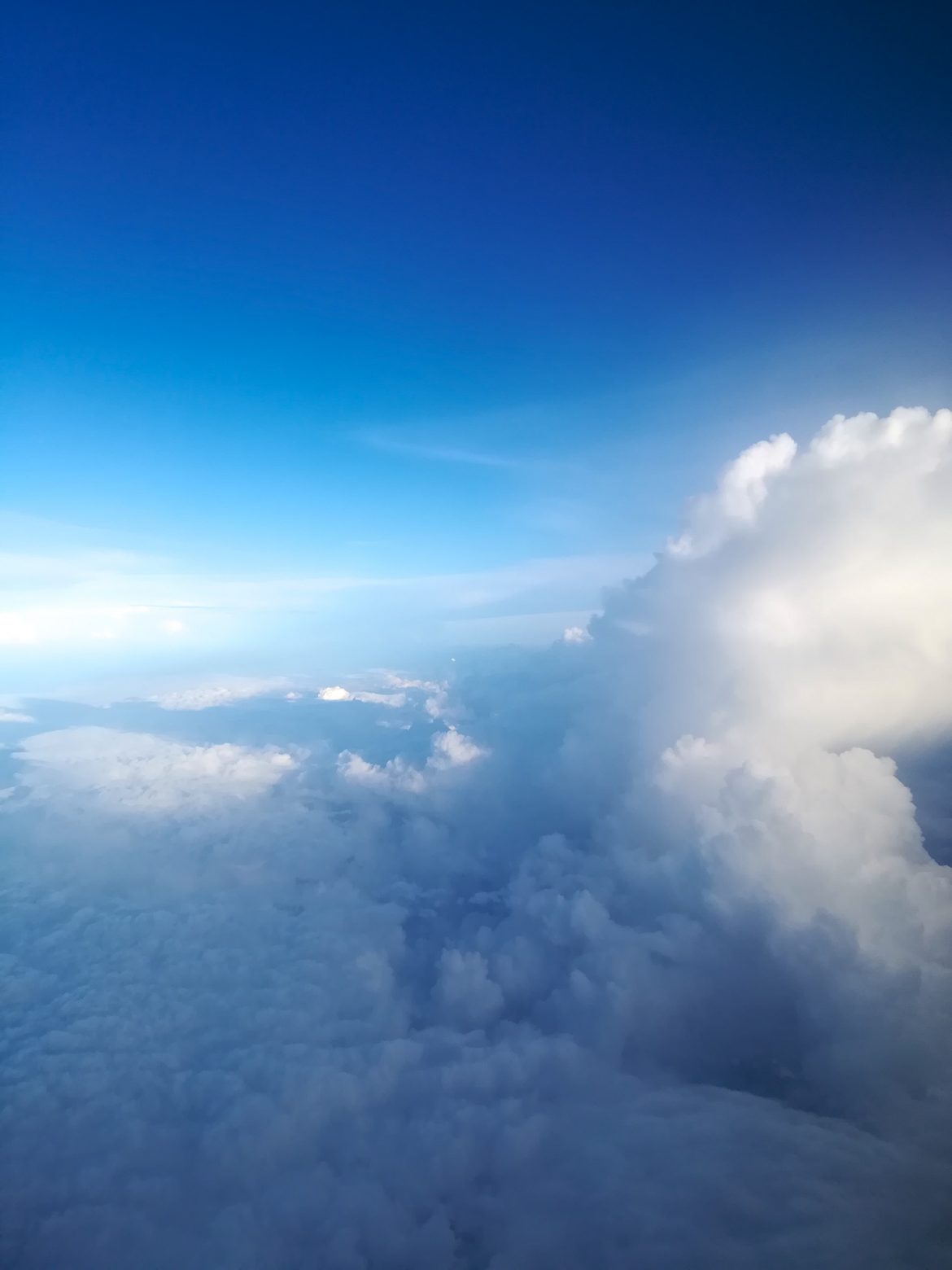 Der Blick aus dem Fenster, während des Fluges. Wolken türmen sich neben dem blauen Himmel auf.
