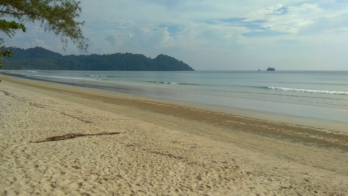 Das seichte Meer trifft auf den hellen Sand des Aow Yai, mit ein paar kleinen Bergen im Hintergrund