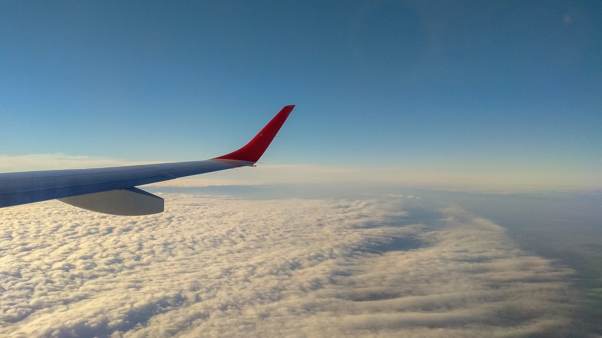 Der Blick aus dem Fenster des Flugzeuges hinab auf Sonne und Wolken