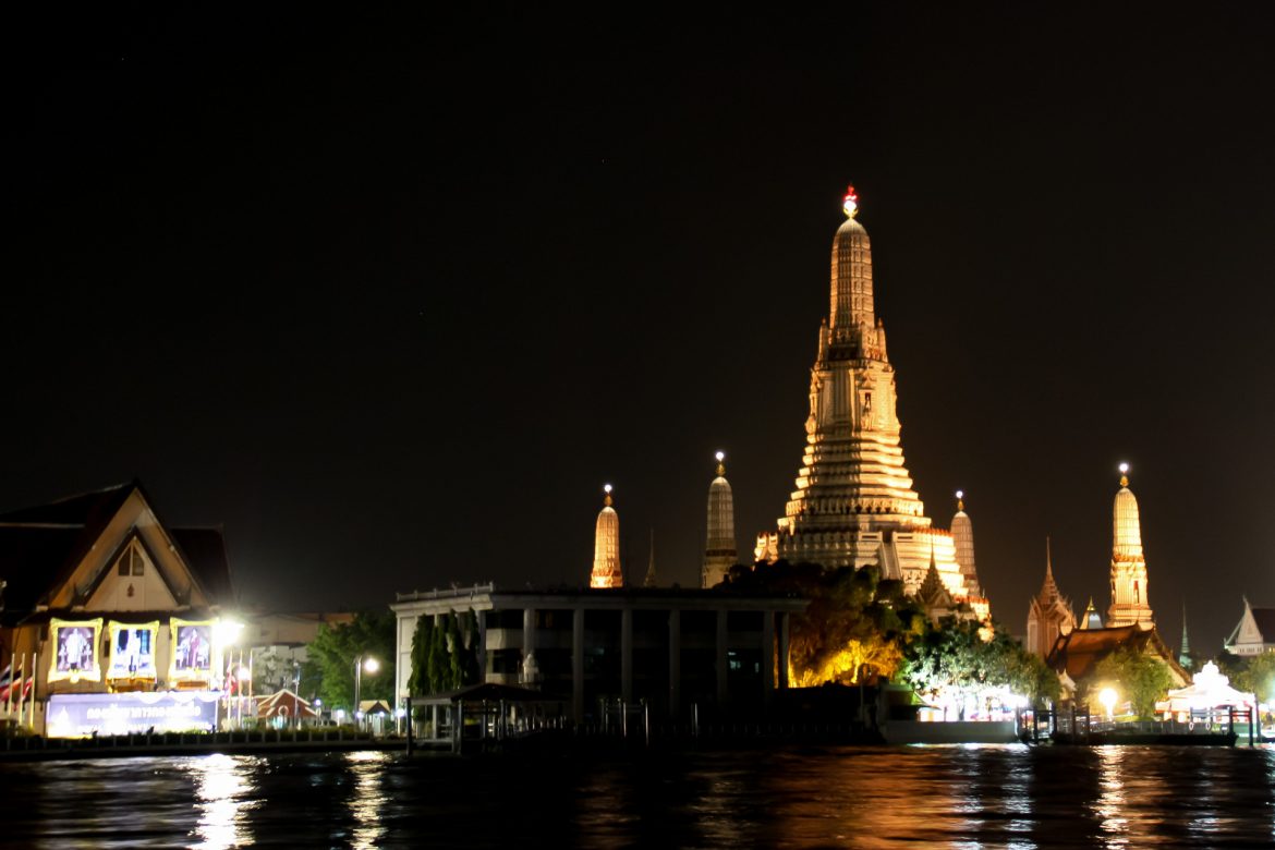 Ein bild vom Wat Arun vor dem Chao Phraya in Bangkok, bei voller Beleuchtung im gelben Schein.