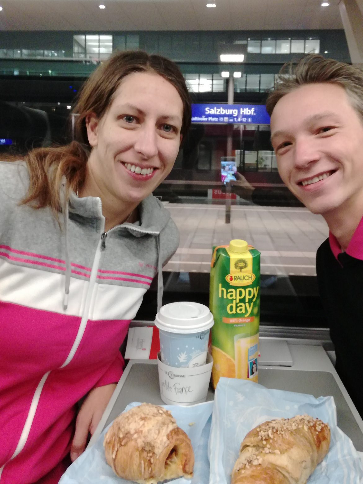 Wir beide zusammen in einem Zug, der gerade am Hauptbahnhof in Salzburg steht, nachdem wir uns dort ein Frühstück vom Bäcker geholt haben.
