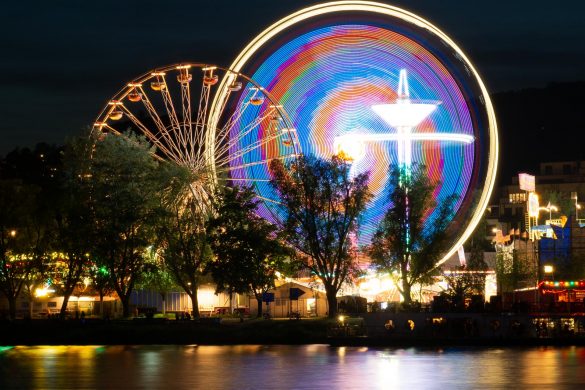 Langzeitbelichtung das still stehende Riesenrad des Urfahraner Marktes in Linz zusammen mit einem hell leuchtenden Fahrgeschäft.