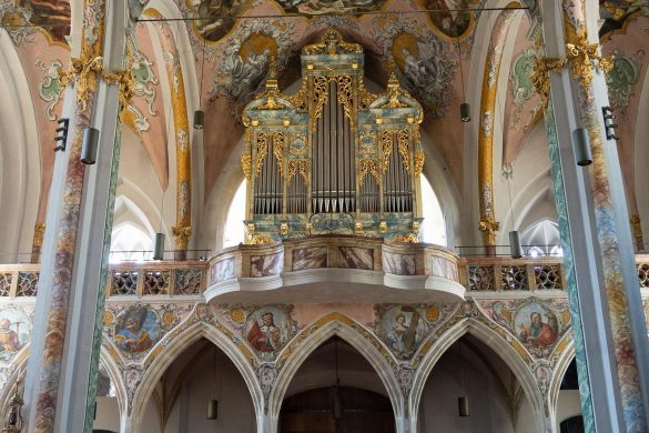 Ein Foto im inneren einer Kirch vom Eingangsbereich, zusammen mit einer großen Orgel darüber und vielen Reihen von Sitzbänken im Vordergrund.