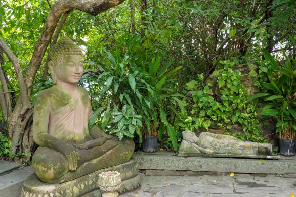 Eine sitzende und eine liegende Buddha Statue mitten in einem kleine Garten im Royal Palace von Phnom Penh