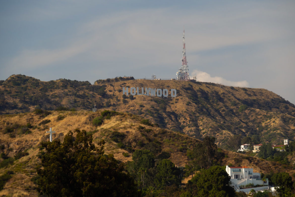 Das Hollywood Sign bei leichten Wolken in der Sonne, mit dem rot-weißen Sendeturm im Hintergrund