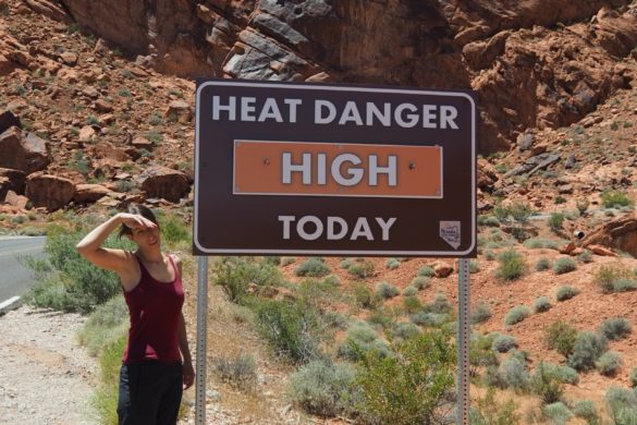 Ein Schild im Valley of Fire, Heat Danger High, mit Anita daneben, die sich bereits den Schweiß von der Stirn wischt.