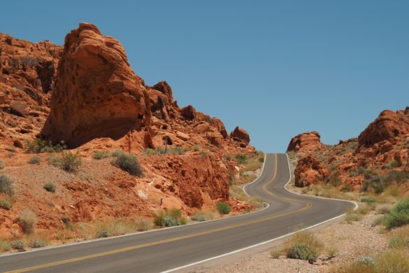 Die Straße schlängelt sich durch das rote, felsige Valley of Fire und verschwindet hinter einem kleinem Hügel am Horizont.
