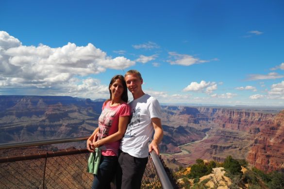 Zusammen lehnen wir an einem Geländer eines Aussichtspunktes des Grand Canyon Nation Parks. Im Hintergrund sieht man den weiten Grand Canyon mit dem darin fließenden Colorado River